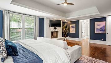 A modern bedroom with a large bed, a fireplace, a TV, and artwork on the walls.