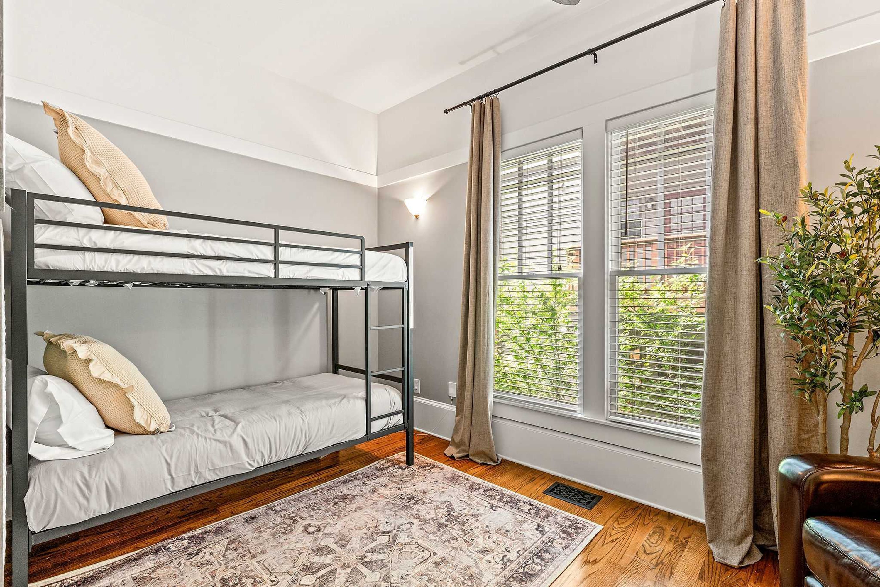 Ein Schlafraum mit Etagenbett, Fenster, Vorhängen und einer Pflanze.