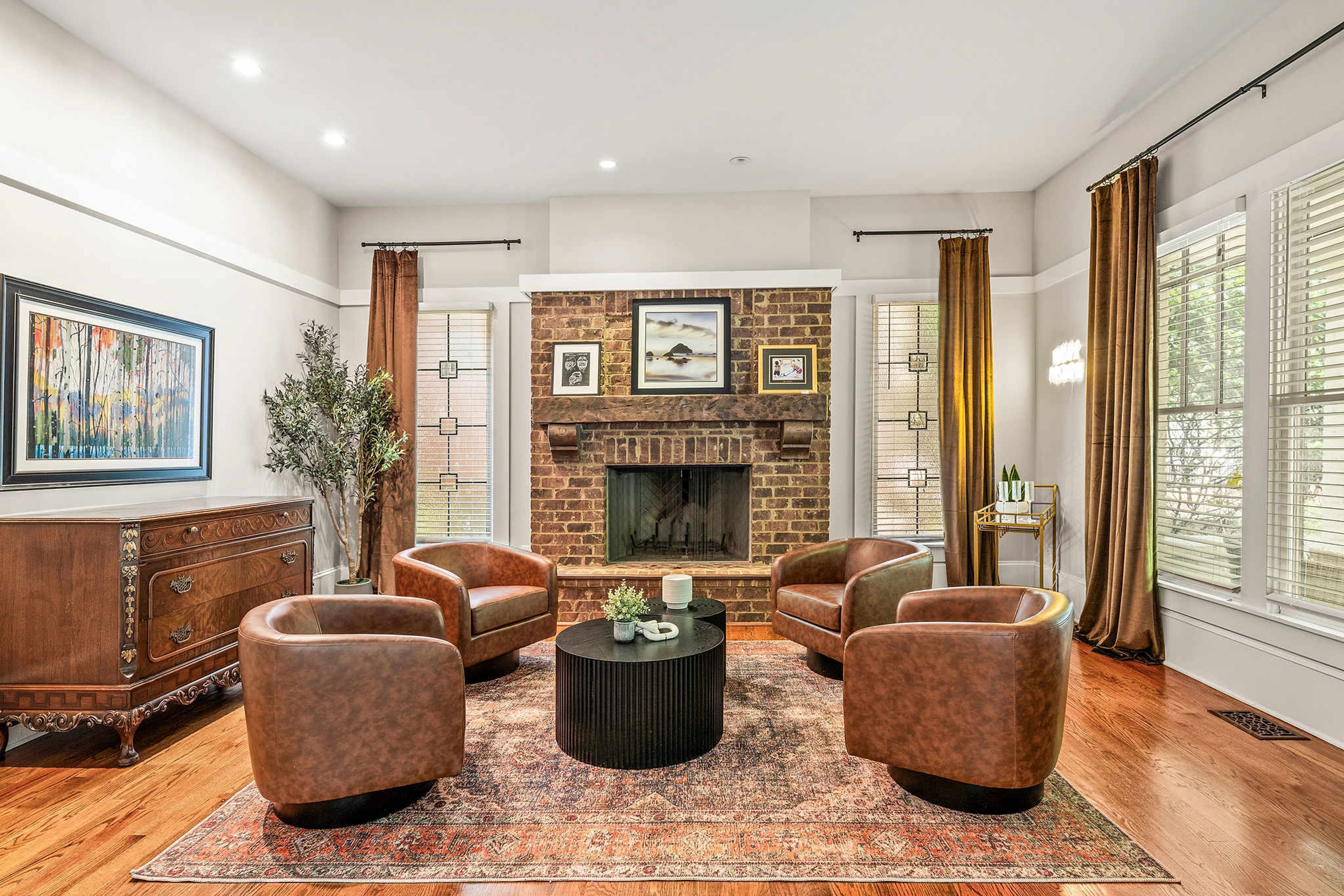 Un salon avec une cheminée en briques, des fauteuils en cuir, une table basse et un grand tableau accroché au mur.
