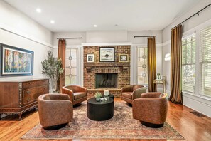 A living room with a brick fireplace, leather armchairs, a coffee table, and a large painting on the wall. - 10 Mins to Mercedes-benz Stadium Dog Friendly (Atlanta)