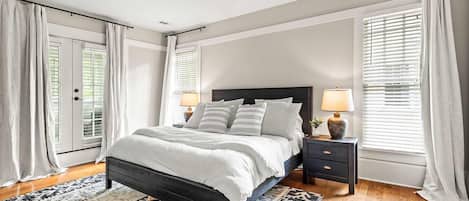 A bedroom with a bed, nightstands, a ceiling fan, and large windows with blinds.