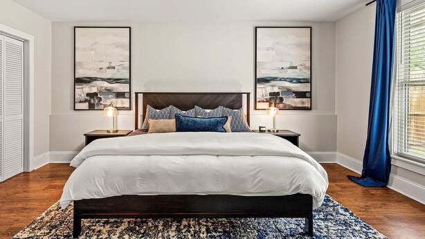Quarto com cama, duas mesas de cabeceira, cabeceira e duas pinturas penduradas na parede.