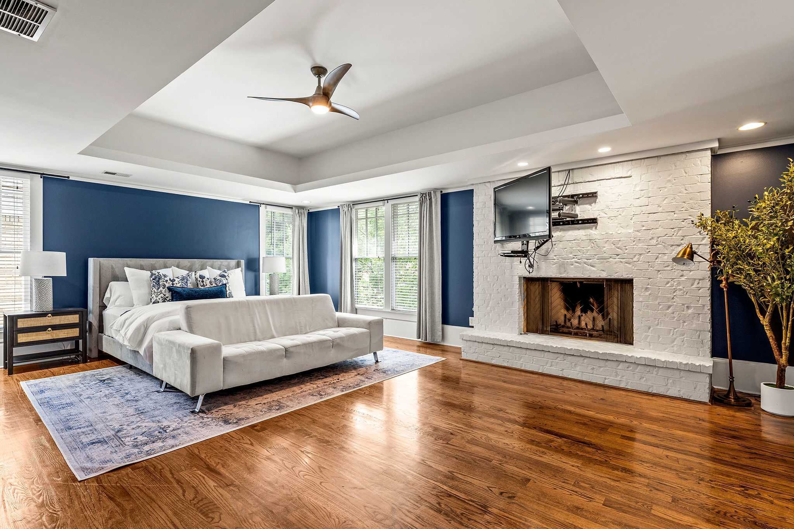 A modern bedroom with a white sofa, a fireplace, and a large window.