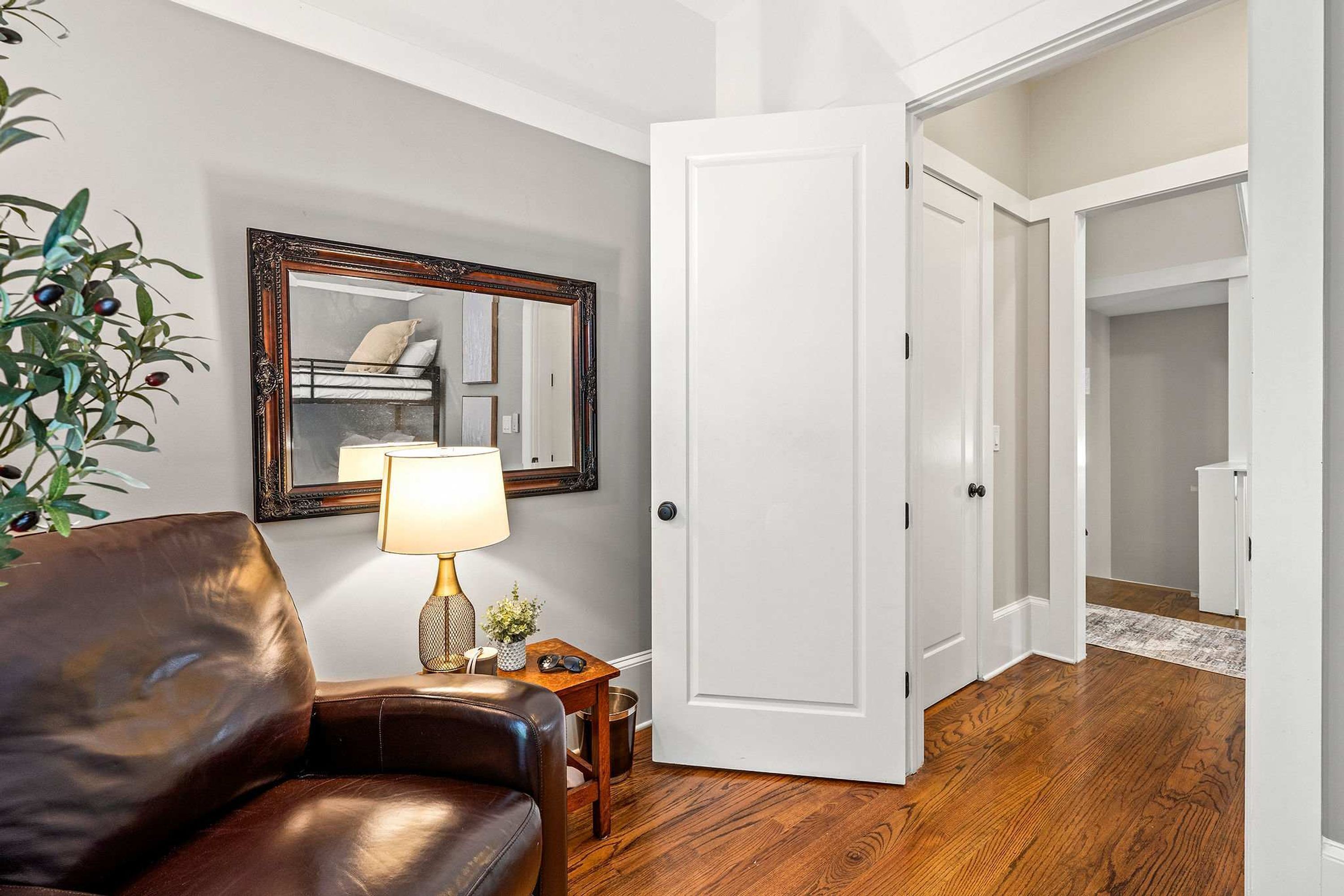 A room with a brown leather chair, a lamp, a mirror, and a door leading to another room.
