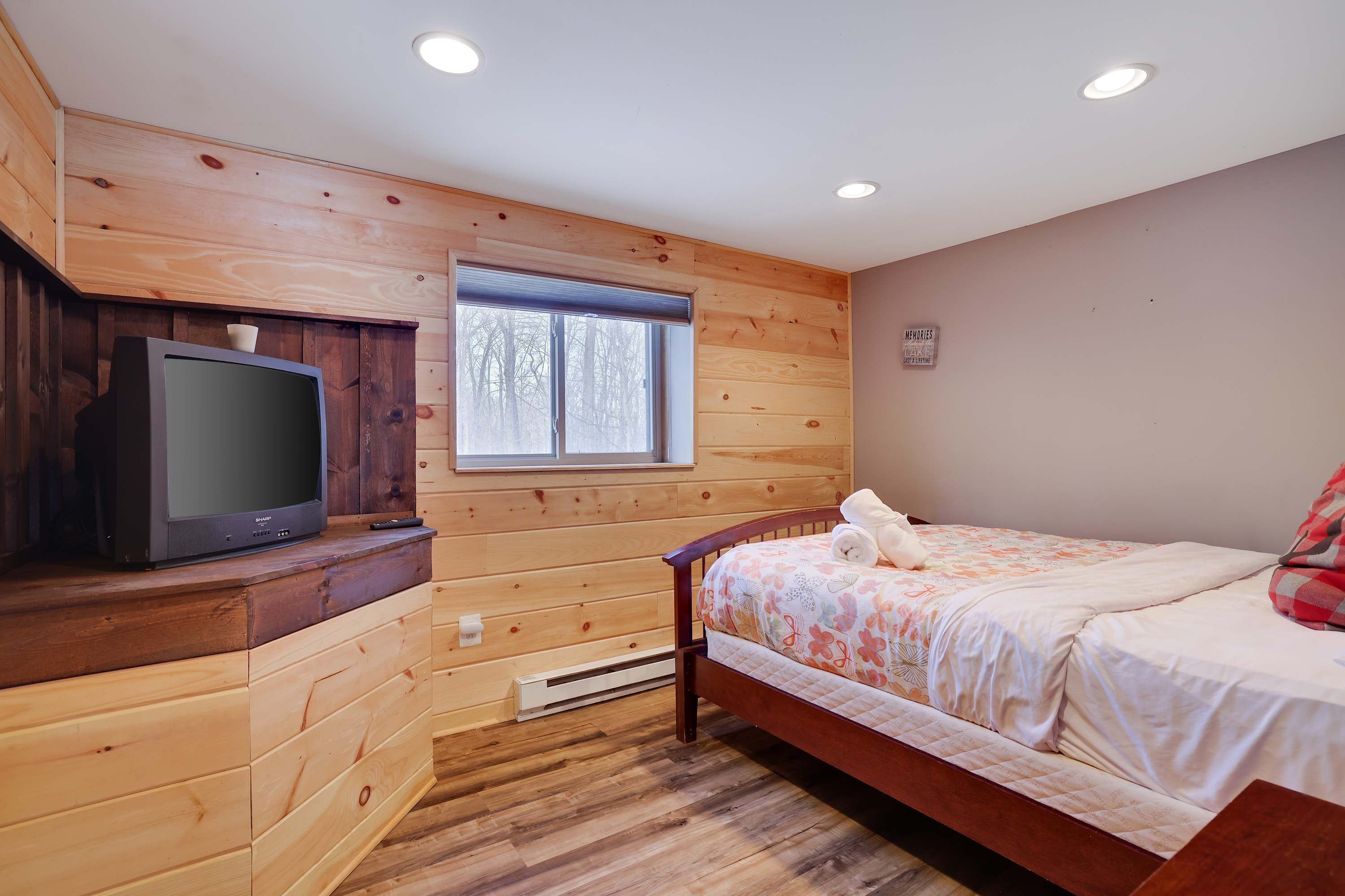 Una habitación de cabaña de madera con una cama, un televisor y una ventana.