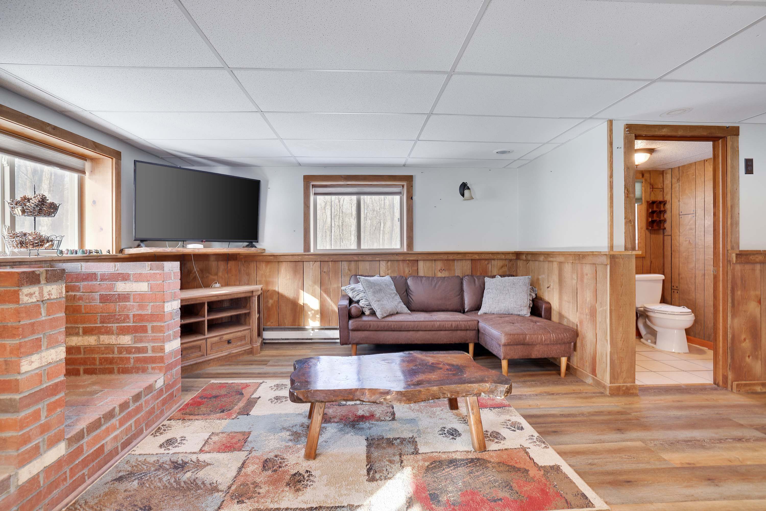 A living room with a television, a brick fireplace, a wooden bench, a sofa, and a patterned rug.