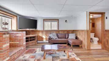 A living room with a television, a brick fireplace, a wooden bench, a sofa, and a patterned rug.