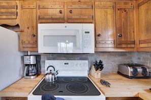 Una cocina con gabinetes de madera, microondas, estufa, cafetera, hervidor, tostadora y un bloque de cuchillos.
