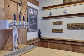 Zona de bar con varias cañas, una pizarra con una fecha y un premio a la cerveza, y estanterías de madera con botellas y carteles.