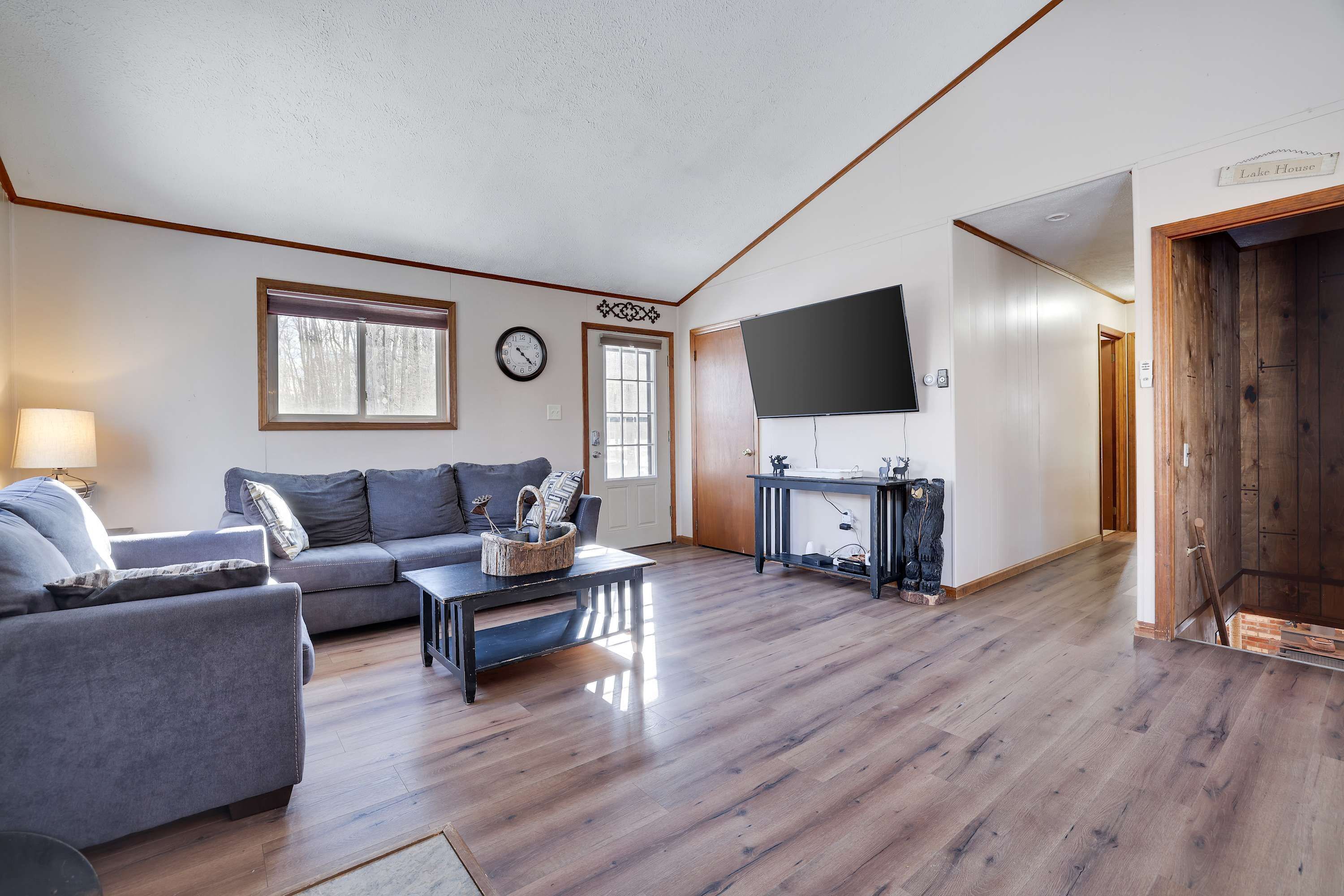 A spacious living room with a grey sofa, a coffee table, and a television mounted on the wall.