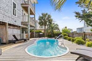 Une terrasse en bois avec un jacuzzi, des chaises longues et une piscine.