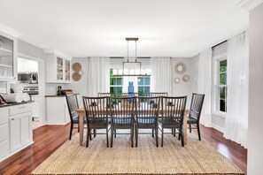 Un espace repas avec une table et des chaises en bois, des murs blancs et une vue sur l’extérieur.