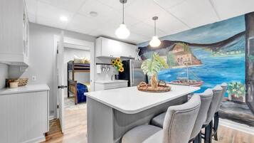 Una cocina moderna con una isla central, asientos tipo barra y un mural que representa una escena costera.
