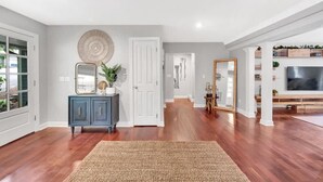 A spacious living room with hardwood flooring, a dark blue cabinet, a large mirror, and a woven rug. - Lakefront Villa Hot Tub Game Room Boat Lift (Mooresville)
