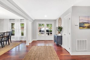 A hallway with a wooden floor, a dining area with chairs, a buffet table, and a large window with a view of greenery. - Lakefront Villa Hot Tub Game Room Boat Lift (Mooresville)