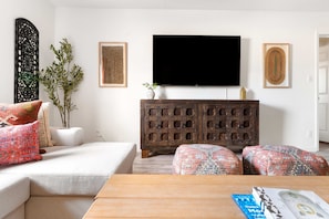 A living room with a sofa, ottomans, a coffee table, a TV, decorative wall panels, and a cabinet. - Sleeps 24 Free Heated Pool Pickleball Theater (Scottsdale)