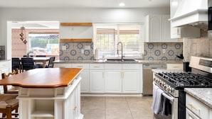 A modern kitchen with white cabinetry, a central island, a built-in stove, and a window with blinds. - Sleeps 24 Free Heated Pool Pickleball Theater (Scottsdale)