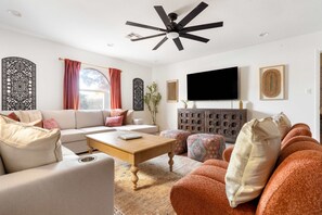 A modern living room with a sofa, ottomans, a coffee table, and a flat-screen TV mounted on the wall. - Sleeps 24 Free Heated Pool Pickleball Theater (Scottsdale)