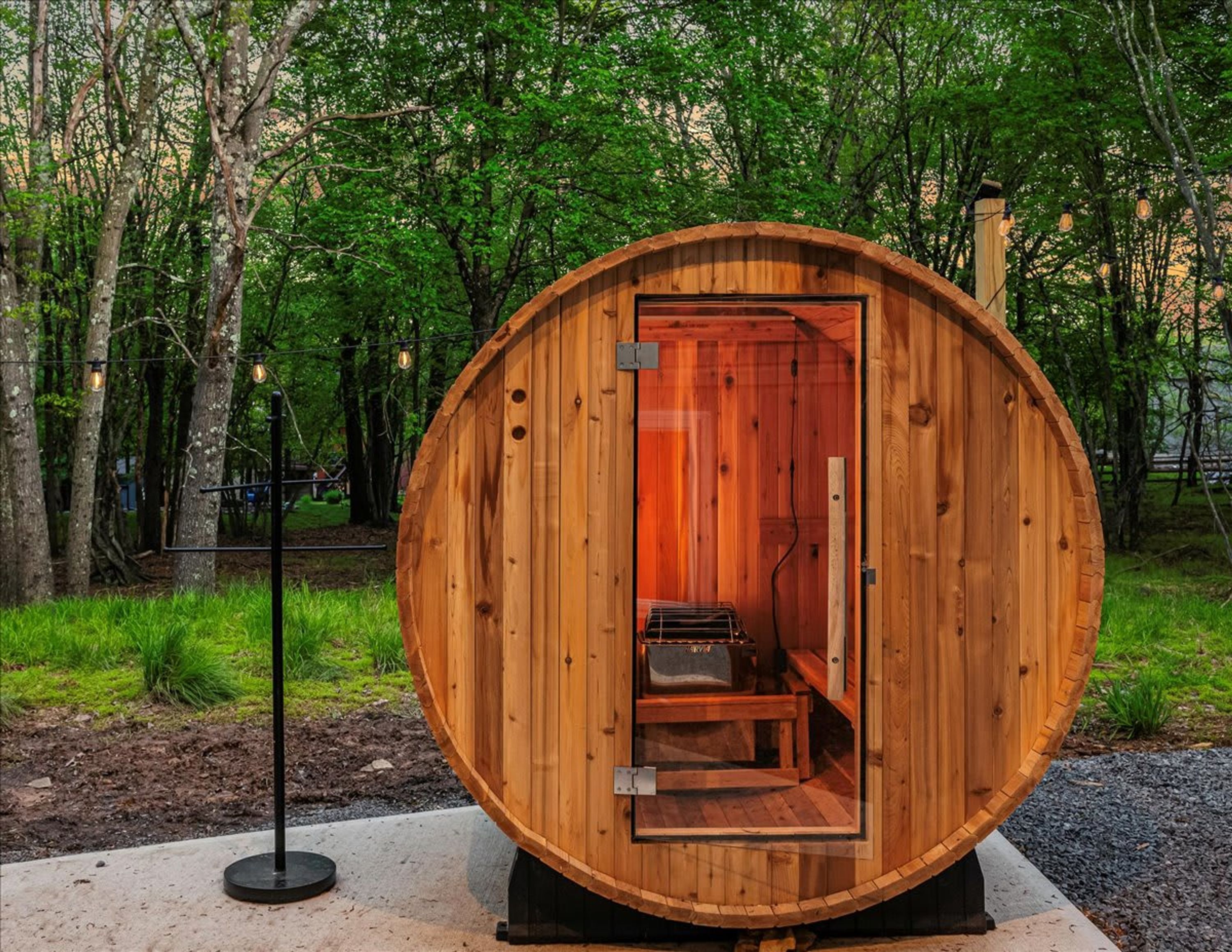 A wooden sauna with a bench and a small table inside, surrounded by trees.