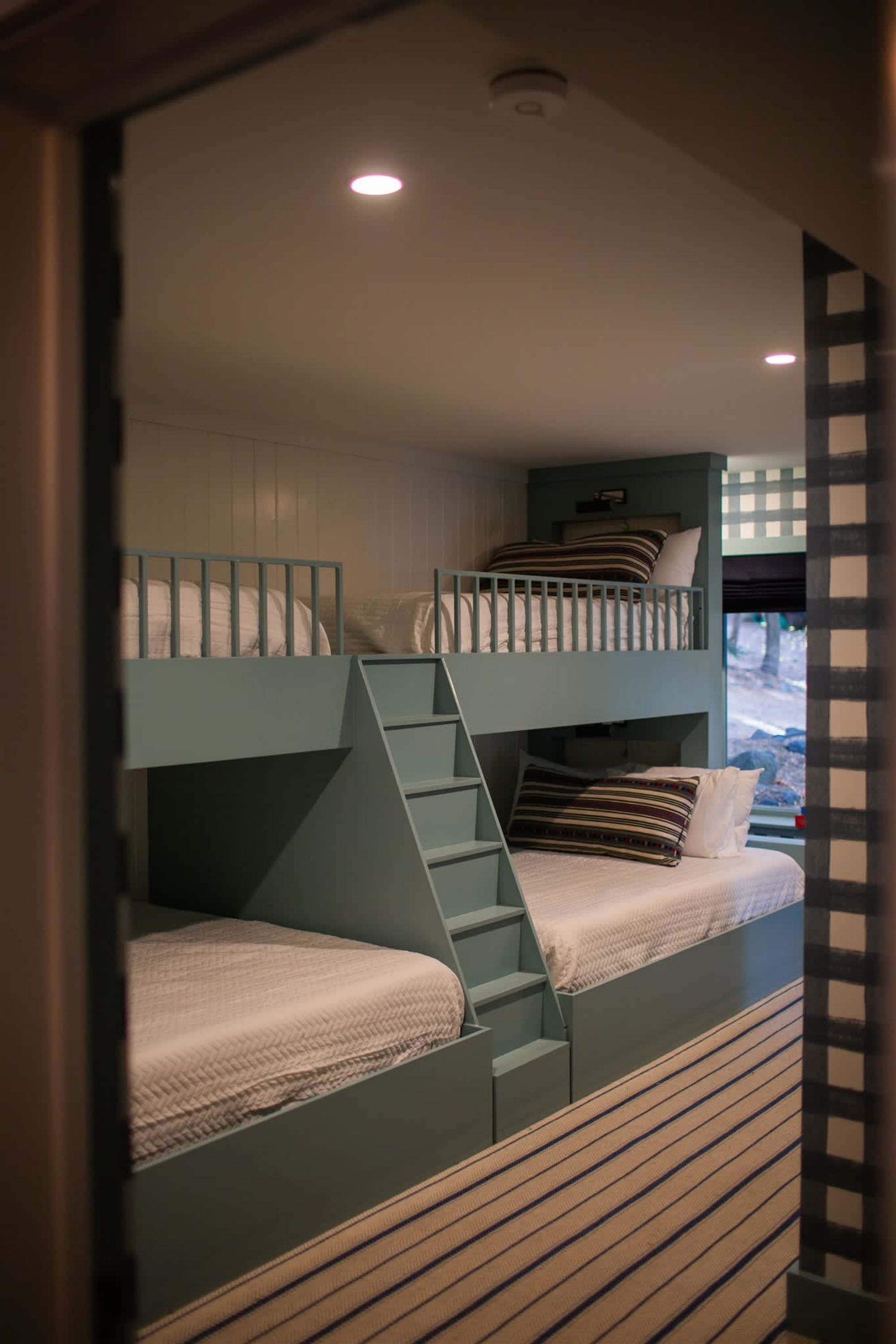 Een slaapkamer met een stapelbed, een ladder naar het bovenste bed, een raam met uitzicht en een plafondlamp.
