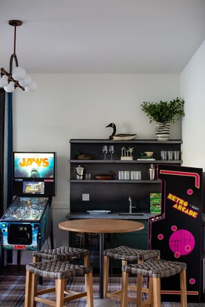 Ein stilvolles Zimmer im Retro-Look mit Spielautomaten, einem Essbereich und einem Regal mit Dekoration.