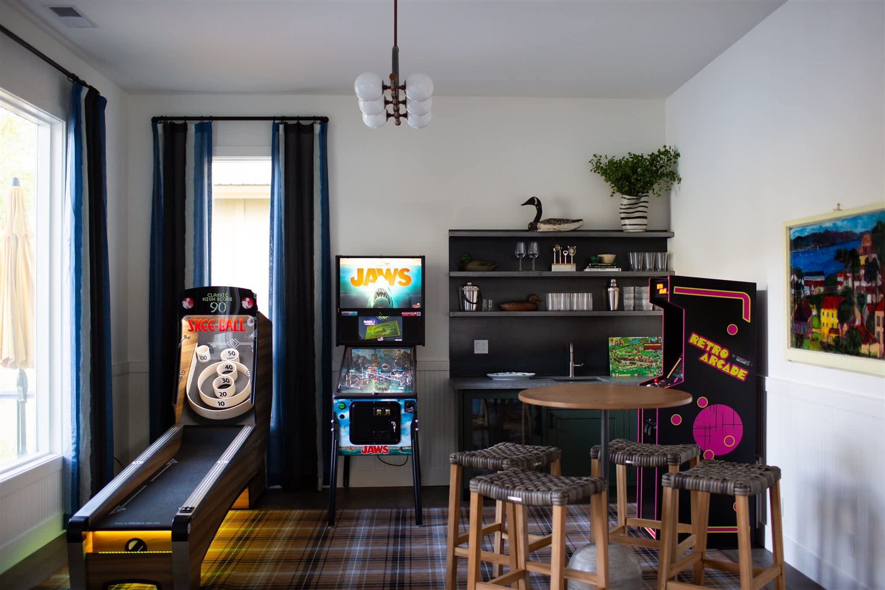 A room with a pinball machine, a jukebox, a retro arcade, and a dining area with stools.