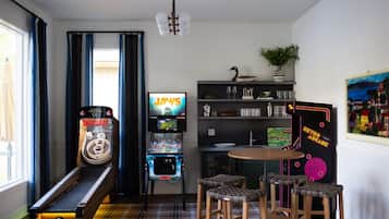 Una habitación con una máquina de pinball, un jukebox, un salón de juegos retro y una zona de comedor con taburetes.