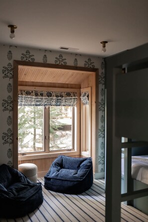 Ein Zimmer mit großem Fenster, Holzboden, einem Sitzsack und einem Etagenbett.