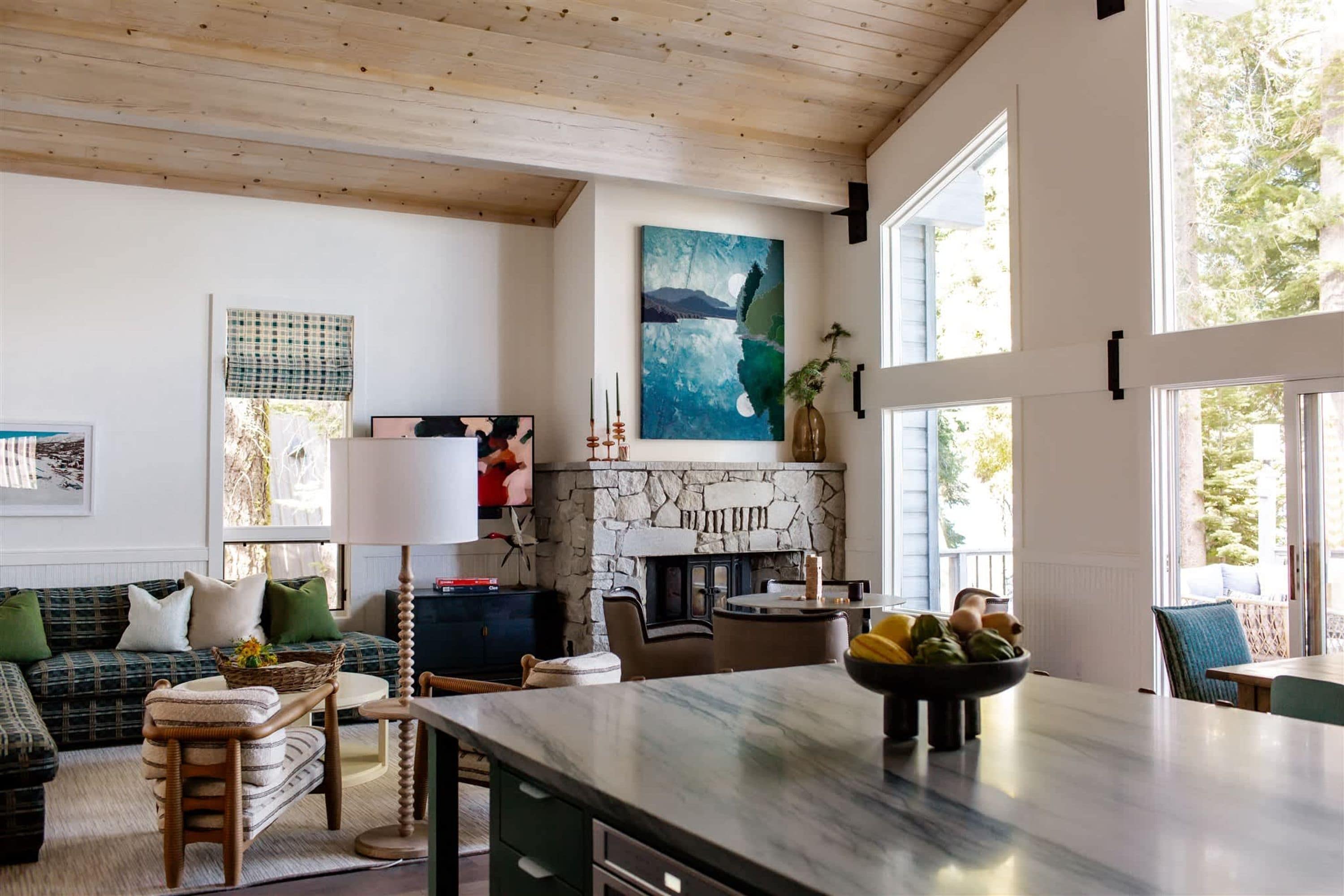 Uma sala de estar ampla com lareira de pedra, uma janela grande e uma cozinha moderna.