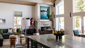 A spacious living room with a stone fireplace, a large window, and a modern kitchen area. - Luxury Lakefront 5 Br Home Hot Tub Arcade (Truckee)