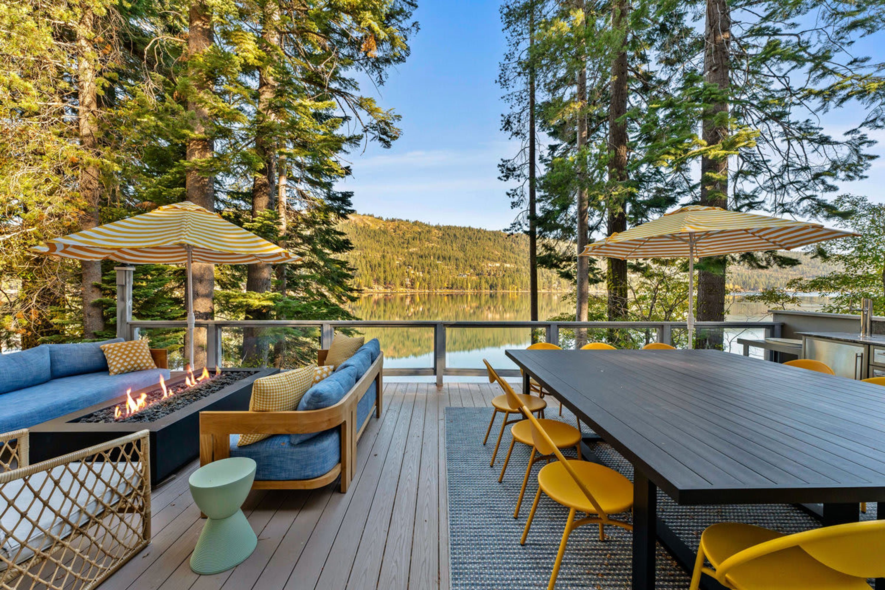 Une terrasse extérieure dotée d’un foyer, d’un espace salon et d’un coin repas, le tout avec vue sur un lac.