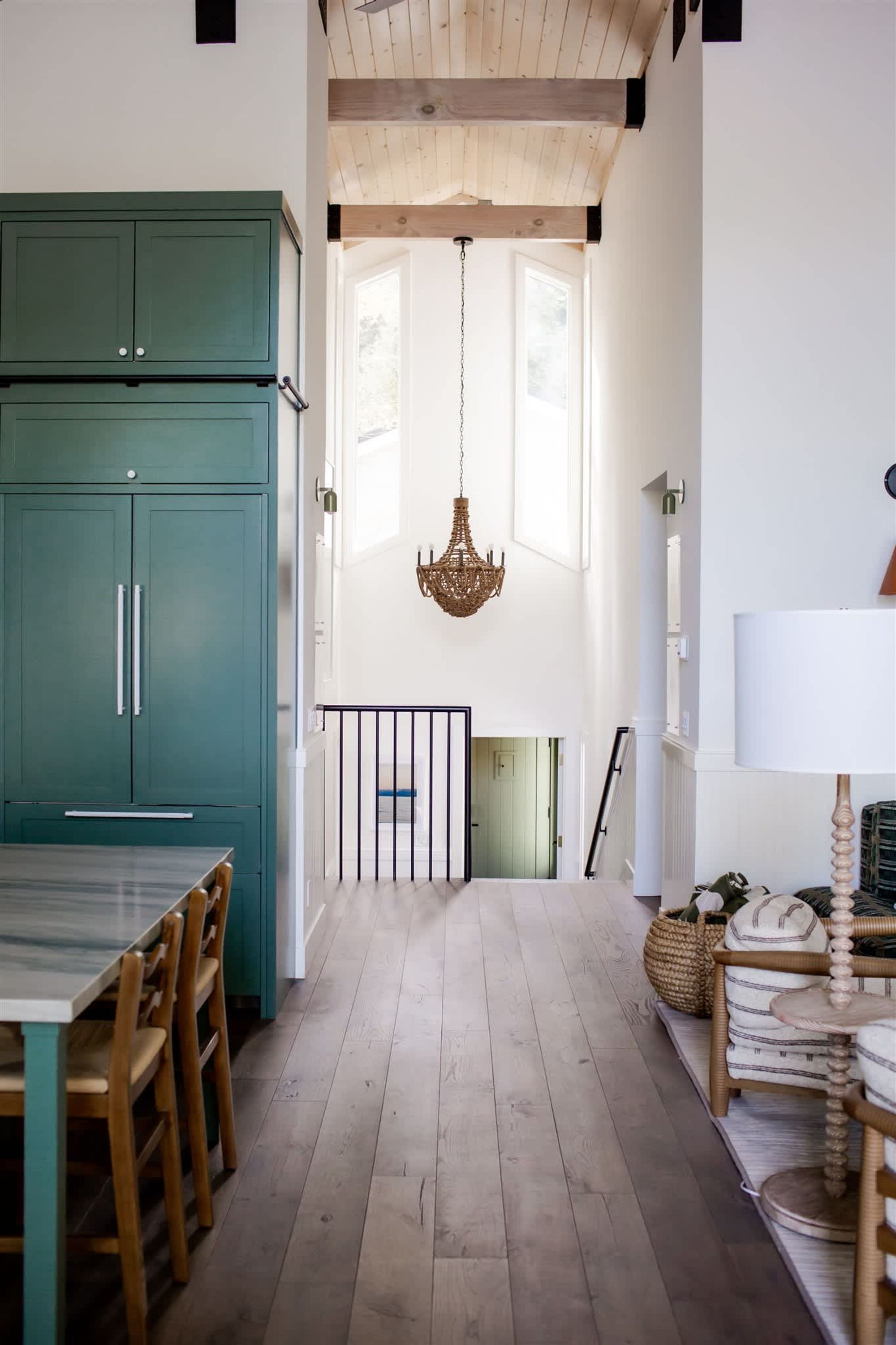 A kitchen with teal cabinets, a dining table with chairs, a chandelier, and a staircase leading to another level.