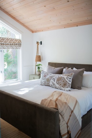 A bedroom with a bed, a nightstand, a lamp, and a window with curtains. - Luxury Lakefront 5 Br Home Hot Tub Arcade (Truckee)