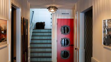 Un pasillo con una escalera que conduce a una habitación con una puerta roja y tres ventanales circulares.