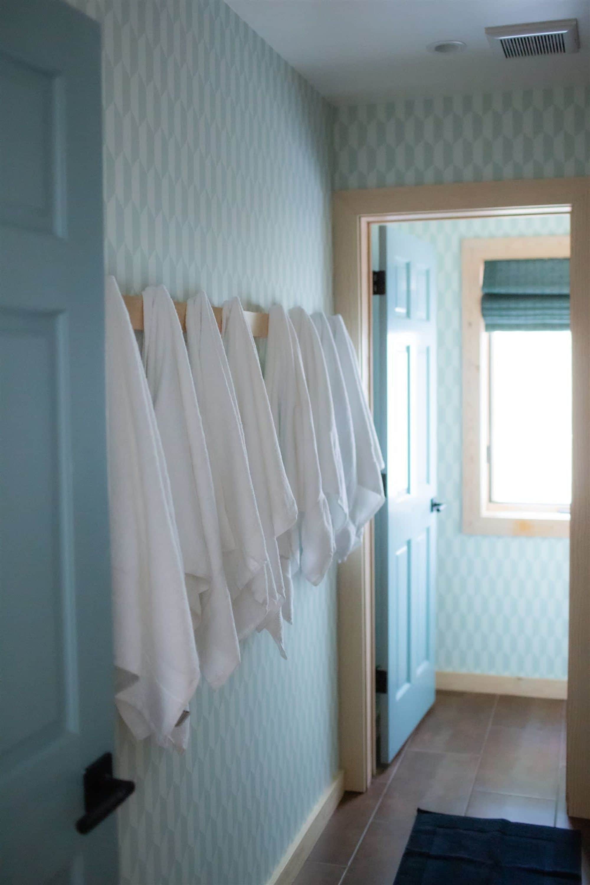 A hallway with a patterned wall and a rack of white towels.