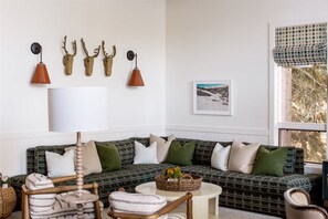 Ein Wohnzimmer mit einem grün gemusterten Sofa, einer weißen Lampe und Wandtaxidermie von Hirschgeweihen.