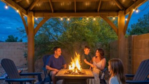 A covered outdoor seating area with a fire pit, surrounded by chairs and tables. - Desert Retreat Pool Fire Pit Family Games (Surprise)