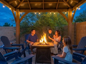 A covered outdoor seating area with a fire pit, surrounded by chairs and tables. - Desert Retreat Pool Fire Pit Family Games (Surprise)