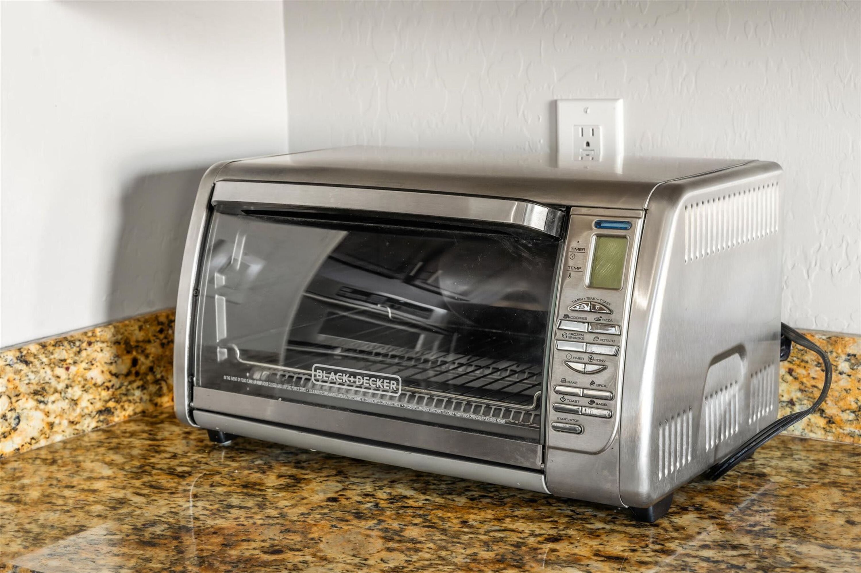 A toaster oven with a digital display and multiple cooking settings on a granite countertop.