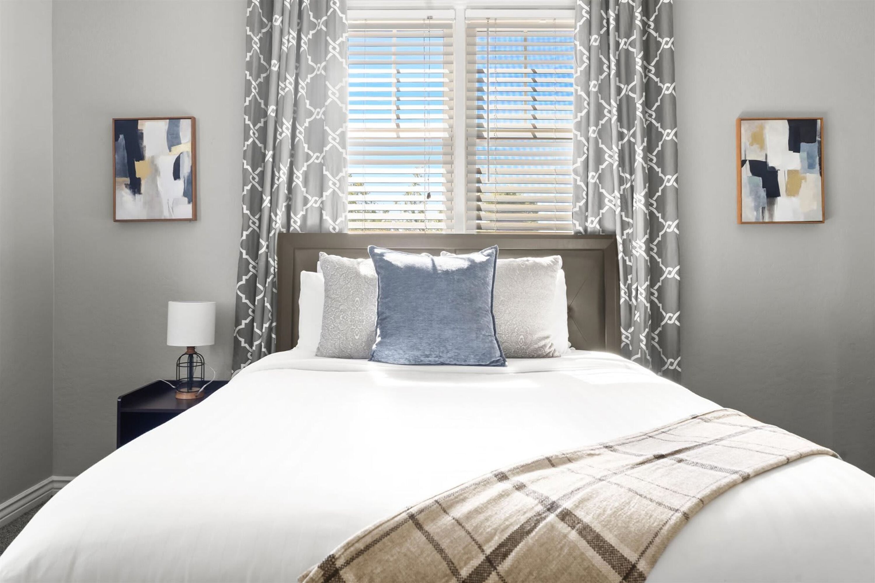 A bedroom with a bed, a nightstand, a lamp, and two paintings on the walls.