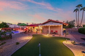 Ein Wohnhaus mit Swimmingpool, überdachter Terrasse und einem kleinen Putting-Green.