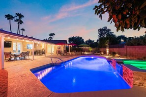 Ein Swimmingpool mit beleuchtetem Rand, Sitzgelegenheiten im Freien mit Sonnenschirmen und ein Gebäude mit Lichterketten.