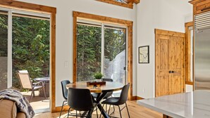 Eine moderne Küche mit großen Fenstern, einem Essbereich mit rundem Tisch und Blick auf einen Wald.