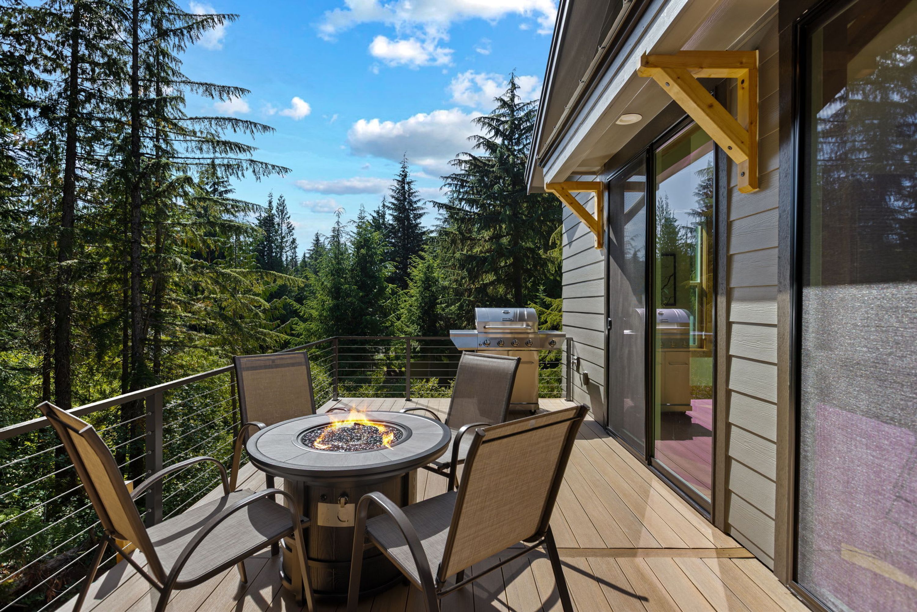 An outdoor deck with a round table and chairs, a grill, and a fire pit.