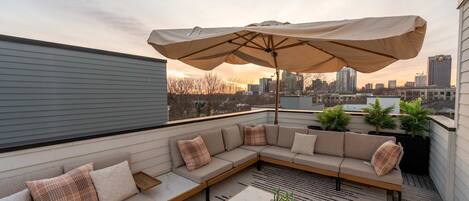 A rooftop patio with a sectional sofa, a coffee table, and an umbrella.
