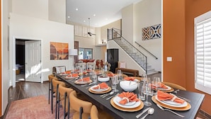 A spacious dining area with a long table set for a meal, a staircase, and a view of the living room. - Luxury 6BR Retreat - Pool BBQ Theater and Games (Mesa)