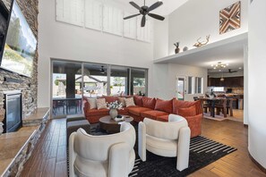 Ein geräumiger Wohnbereich mit Steinwand, einem großen Sofa, zwei Sesseln, einem Couchtisch und Blick ins Freie.