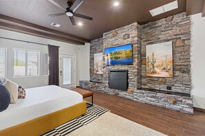 Ein Schlafzimmer mit Bett, Sitzbank, Fernseher an einer Steinwand und Kamin.