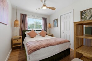 A bedroom with a bed, bedside tables, a ceiling fan, a window with curtains, and wall art. - Poolside Retreat Sleeps 8 Putt Putt Hot Tub (Bradenton)