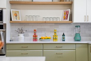 A kitchen with white cabinets, a wooden shelf, and various kitchen items including a blender, a bowl of lemons, and a container of utensils. - Poolside Retreat Sleeps 8 Putt Putt Hot Tub (Bradenton)